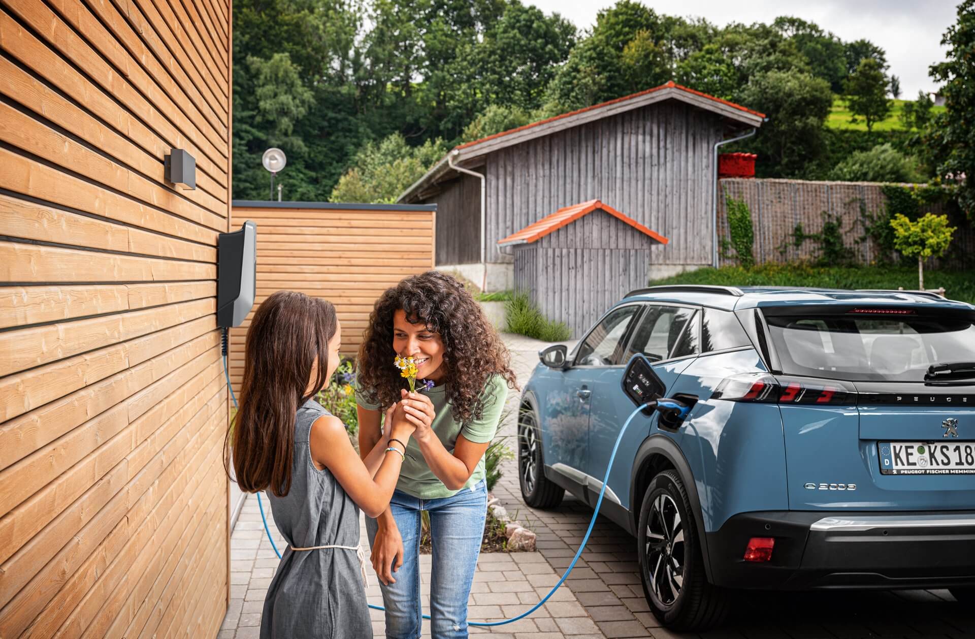 Kind schenkt Mutter Blumen, im Hintergrund wird ein E-Auto geladen