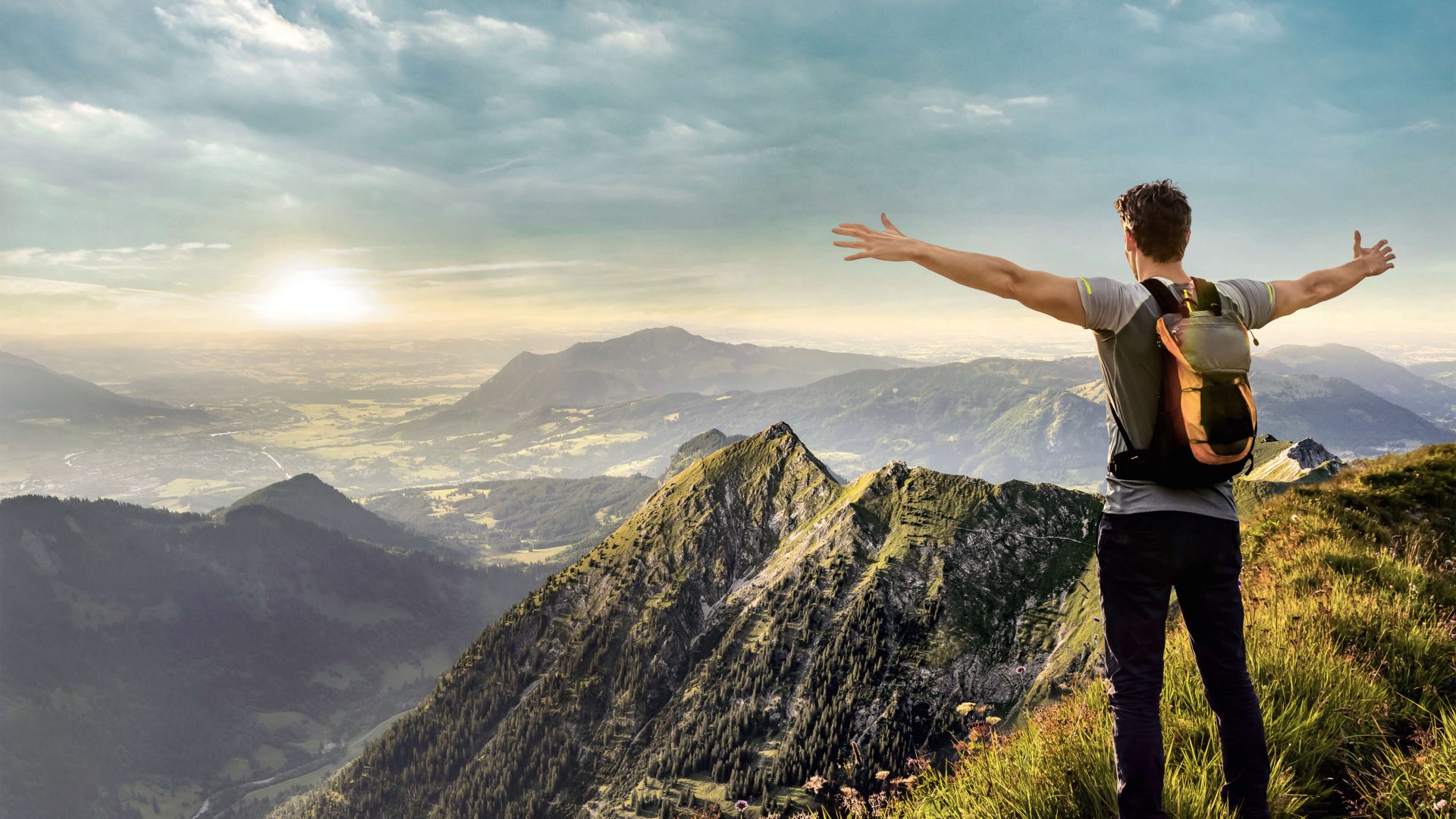Wanderer streckt die Arme in die Luft mit Ausblick auf eine Berglandschaft